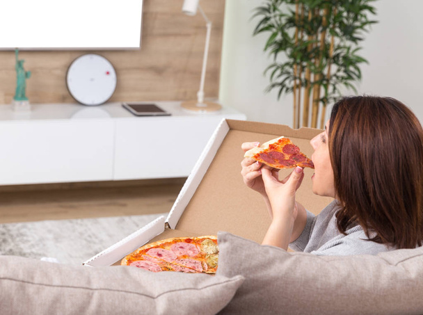 Alleenstaande vrouw eten van pizza en tv kijken - Foto, afbeelding