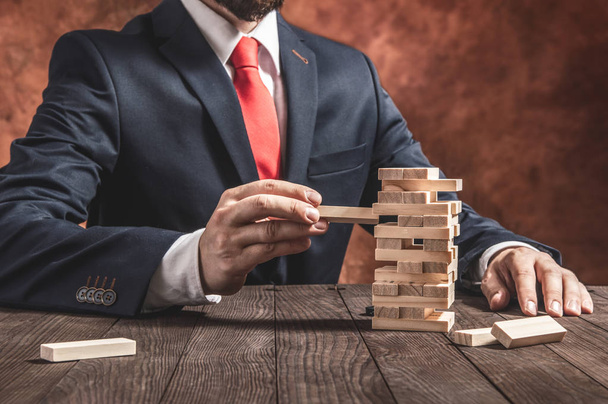 Businessman pulls out blocks from wooden tower. Conception of balance and planning in business. - Fotoğraf, Görsel