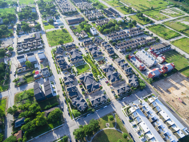 Вид с воздуха на окрестности жилых домов в пригородной зоне Хьюстона, штат Техас, США. Плотно упакованные дома, подъездная дорога окружена зелеными деревьями, пролетающими рано утром. Развитие жилищного строительства
 - Фото, изображение