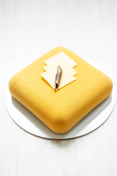 優雅な正方形のベロアのムースケーキ。ナットおよびフルーツの内部充填します。現代的な黄色のパイ。選択と集中。白いテーブル. - 写真・画像