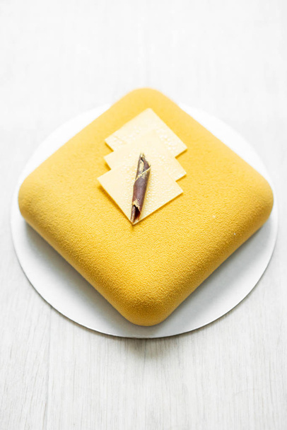 優雅な正方形のベロアのムースケーキ。ナットおよびフルーツの内部充填します。現代的な黄色のパイ。選択と集中。白いテーブル. - 写真・画像