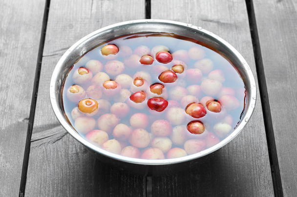 bol en métal avec des cerises colorées dans l'eau sur un fond de table gris en bois, vue latérale
 - Photo, image
