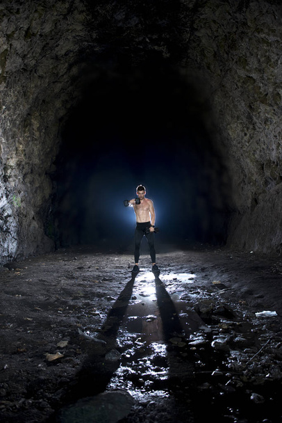 Forte jovem macho levantando halteres em uma caverna
 - Foto, Imagem