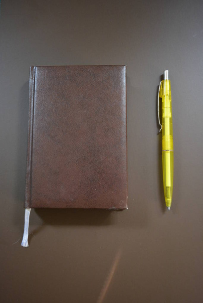 Brown book diary with a yellow pen on a brown matte background. - Photo, image