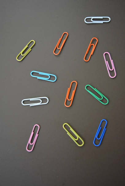 clips de color de diferentes colores se dispersan y clips multicolores se extienden sobre un fondo marrón mate
. - Foto, imagen