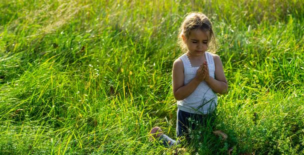 Mała dziewczynka zamknęła oczy modląc się o zachodzie słońca. Ręce złożone do modlitwy pojęcie wiary, duchowości i religii. Nadzieja, koncepcja. - Zdjęcie, obraz