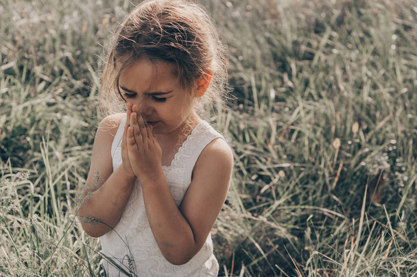 Klein meisje haar ogen bidden bij zonsondergang gesloten. Handen gevouwen in gebed concept voor geloof, spiritualiteit en religie. Hoop, concept. - Foto, afbeelding