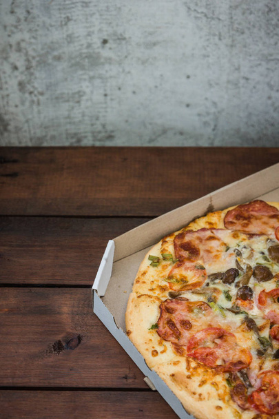 Italian pizza in a cardboard box. Pizza on wooden background in rustic style. Simple food on a wooden background. Tasty dish for lunch - Photo, image