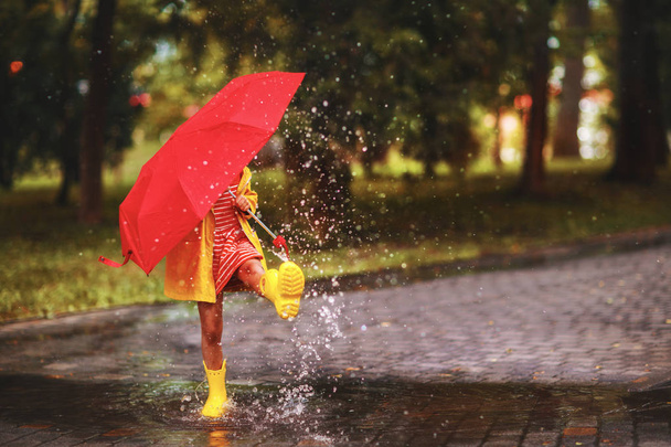 gelukkig kind meisje met een paraplu en rubber laarzen in plas op een herfst wal - Foto, afbeelding