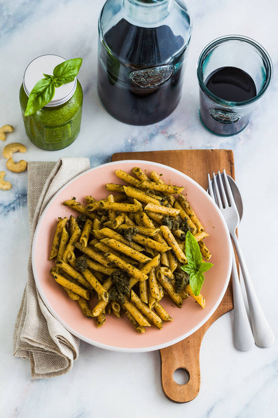 wholemeal pasta with basil pesto in dish on table with red wine. light Mediterranean dish. vegan healthy food - Photo, Image