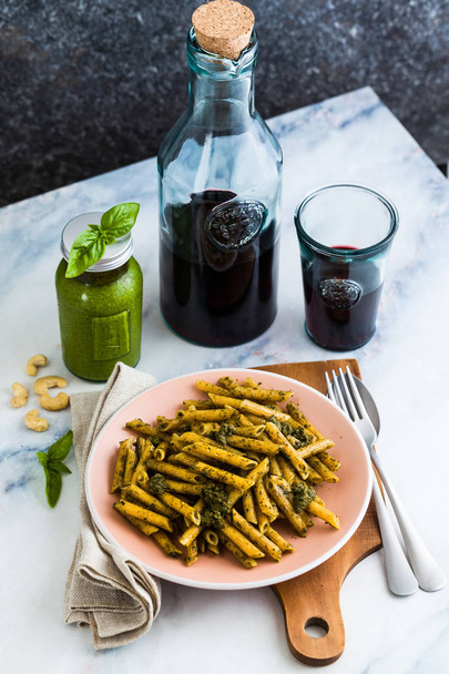 wholemeal pasta with basil pesto in dish on table with red wine. light Mediterranean dish. vegan healthy food - Foto, Bild