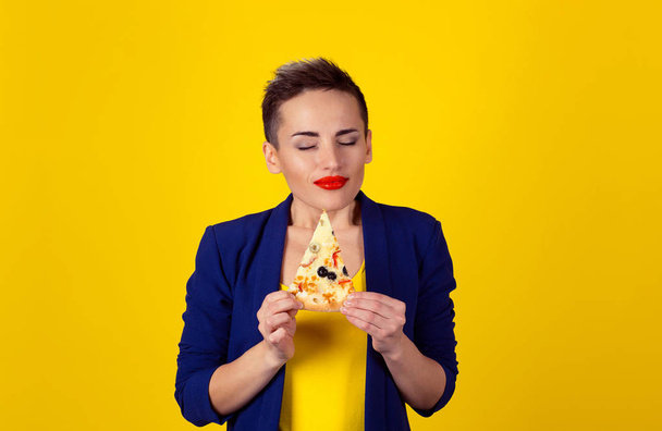 Closeup portrait young woman holding, fatty pizza eyes closed of pleasure, enjoying the smell and craving junk food not trying to resist temptation isolated yellow background. Positive face expression - Фото, зображення