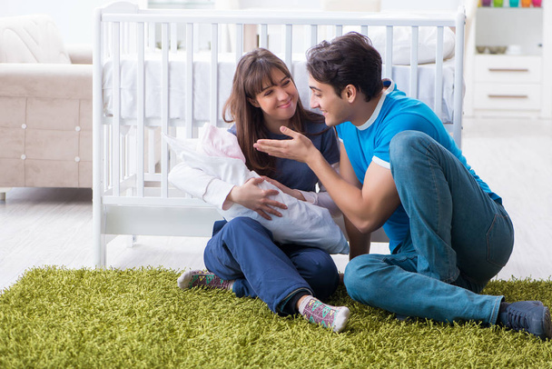 Mladí rodiče se svým novorozeným dítětem sedí na koberci  - Fotografie, Obrázek