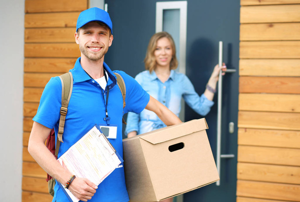 Smiling delivery man in blue uniform delivering parcel box to recipient - courier service concept. Smiling delivery man in blue uniform - Фото, изображение