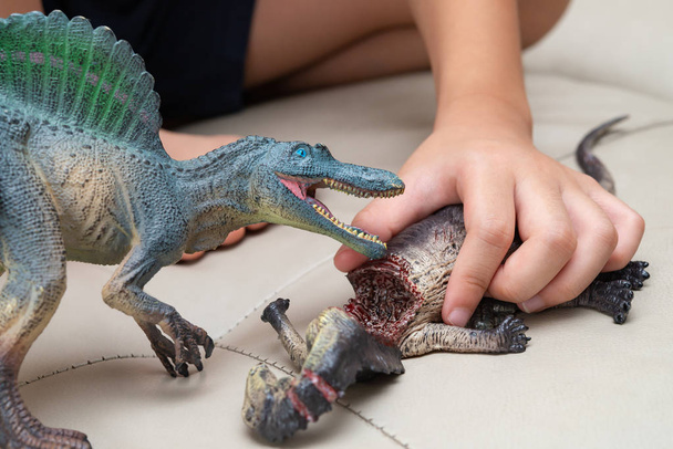 Kind spielt mit Spielzeug von Spinosaurus und Dinosaurier blutigen Körper auf Sofa zu Hause - Foto, Bild