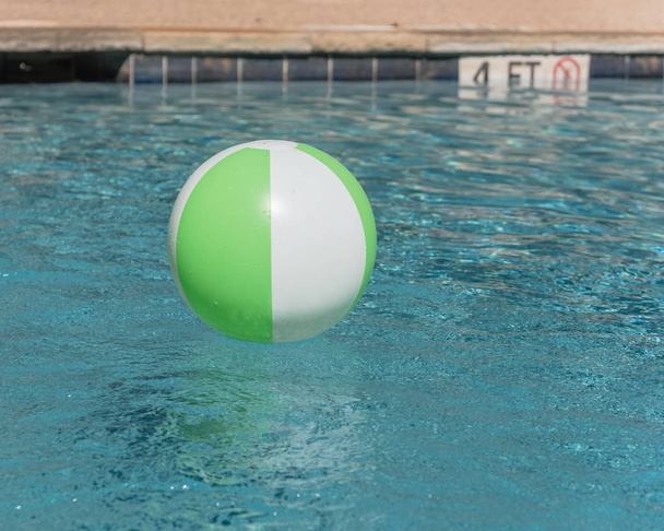 Крупный план ярко-зеленый пляжный мяч возле бассейна справляется края с глубиной и не дайвинг знак. Плавание в освежающей голубой воде с волнами, отражающимися на летнем солнце возле бассейна
 - Фото, изображение