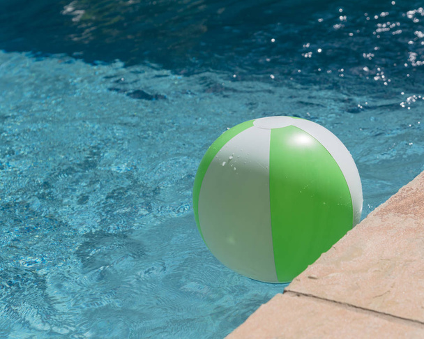 Крупним планом вид зверху один яскраво-зелений пляжний м'яч біля басейну копіює край. Плаває в освіжаючій блакитній воді з хвилями, що відображаються на літньому сонці біля палуби басейну та плитки. Рятувальник для дитини
 - Фото, зображення
