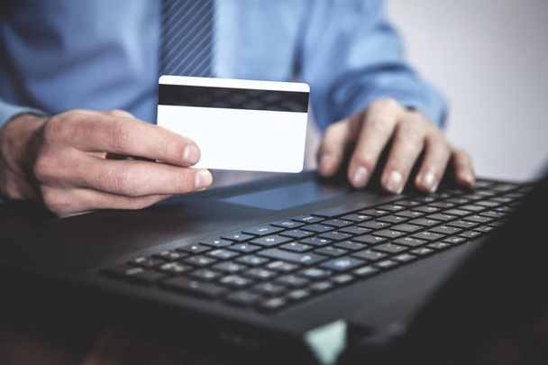 Mies käyttää kannettavaa tietokonetta ja näyttää luottokorttia. Liiketoiminta
 - Valokuva, kuva