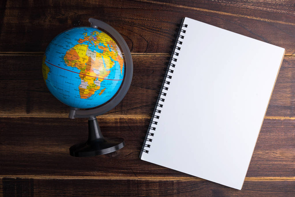 Top view of Blank notebook white paper and globe world map on blue wooden background with space for your message - Photo, Image