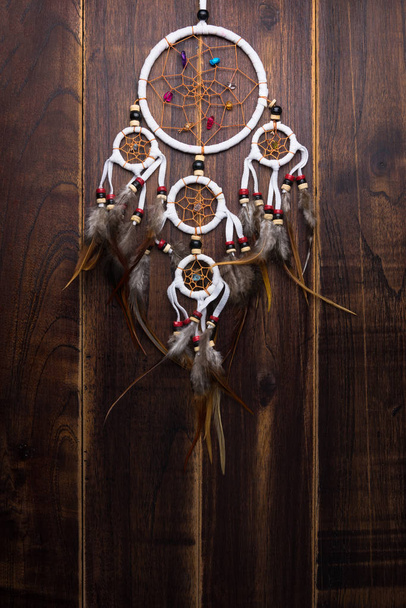 Dream catcher with feathers threads and beads rope hanging spiritual folk american native indian amulet isolated on brown wooden textured background.Concept prevent evil in Halloween - Photo, Image