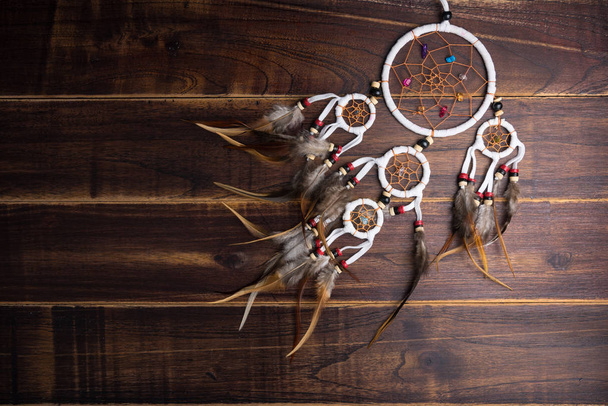 Dream catcher met veren threads en kralen touw opknoping spirituele folk Amerikaanse inheemse Indiaanse amulet geïsoleerd op bruin houten gestructureerde achtergrond. Concept voorkomen kwaad in Halloween - Foto, afbeelding