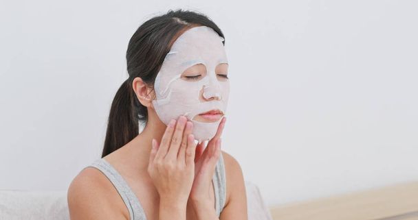 Woman apply facial paper mask on face at home - Foto, afbeelding