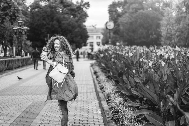 girl with curly hair walking at street with coffee cup and smiling, black and white - Foto, imagen