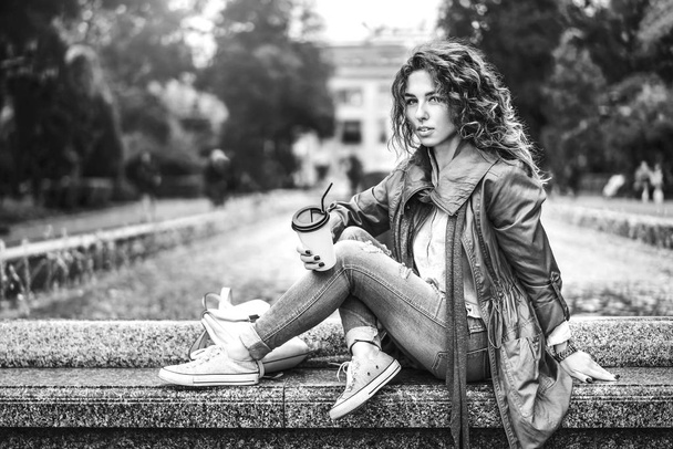 girl with curly hair posing at fountain with coffee cup, black and white - Foto, imagen