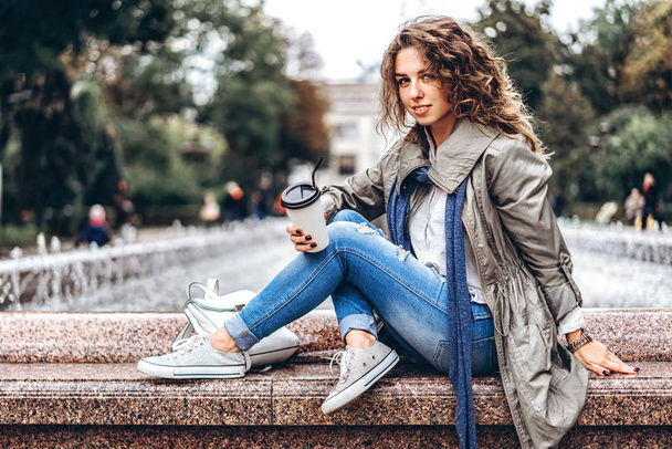 girl with curly hair posing at fountain with coffee cup - Foto, immagini