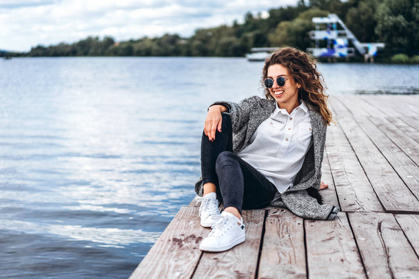 Pretty girl with curly hair posing near lake and smiling - Photo, image