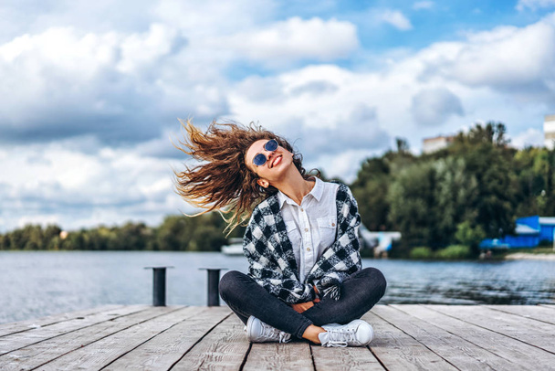 girl with curly hair in sunglasses shaking head near lake and smiling - Foto, Imagem