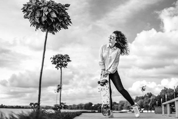 Pretty girl with curly hair posing with skateboard in park, black and white - Foto, immagini