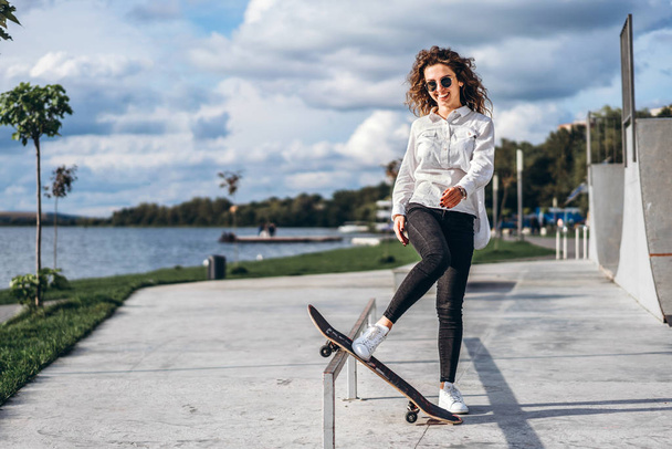 Pretty girl with curly hair posing on skateboard and smiling - Foto, Bild