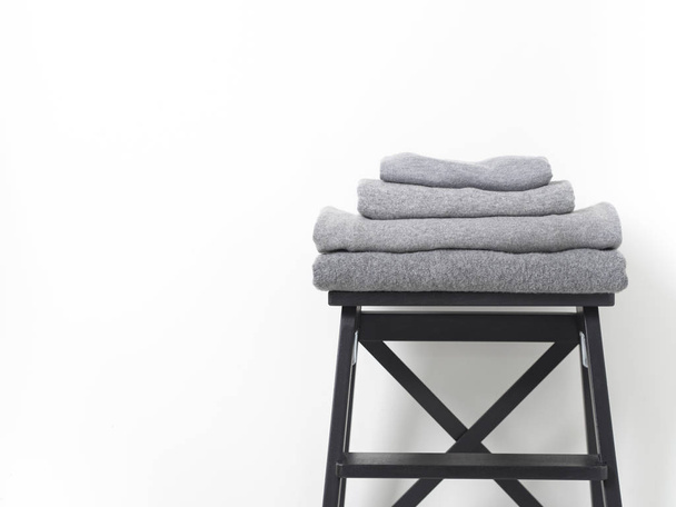 careful stack of grey woolen and cashmere sweaters on wooden stool over white background - Fotoğraf, Görsel