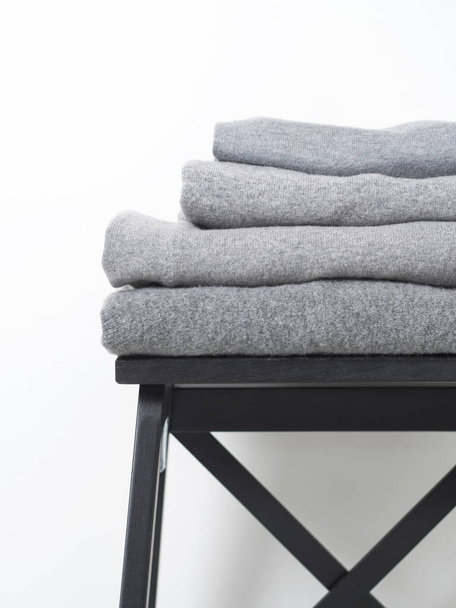 careful stack of grey woolen and cashmere sweaters on wooden stool over white background - Photo, Image