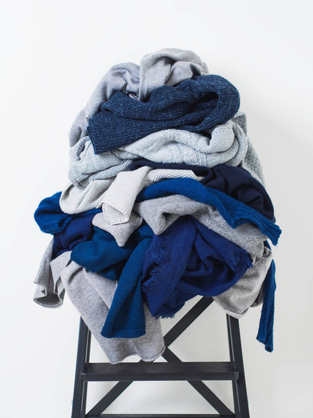 白い背景の上の椅子にグレーとブルーのウール セーターの乱雑な杭 - 写真・画像