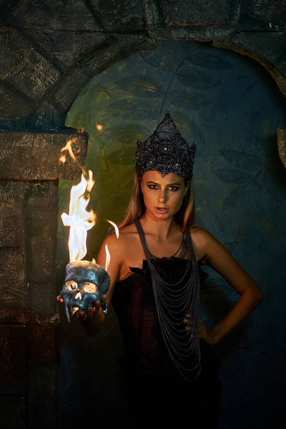 girl in gothic costume holds a burning skull - Фото, изображение