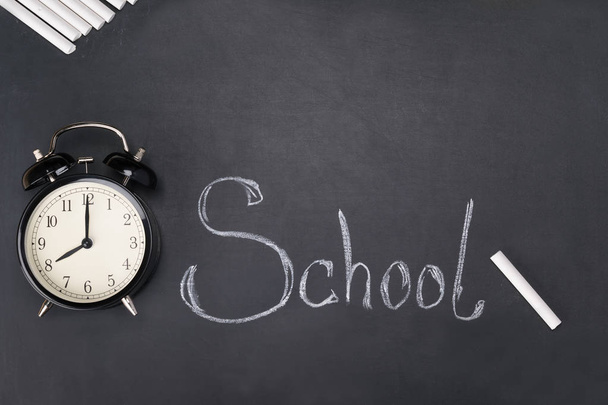 the alarm clock and chalk lies on the board on which the word school is written - Foto, Imagen