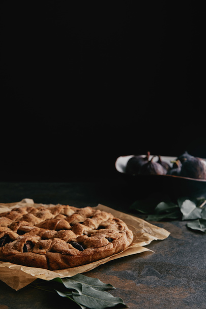 close up view of homemade pie on baking paper and fresh figs on dark tabletop - Фото, изображение