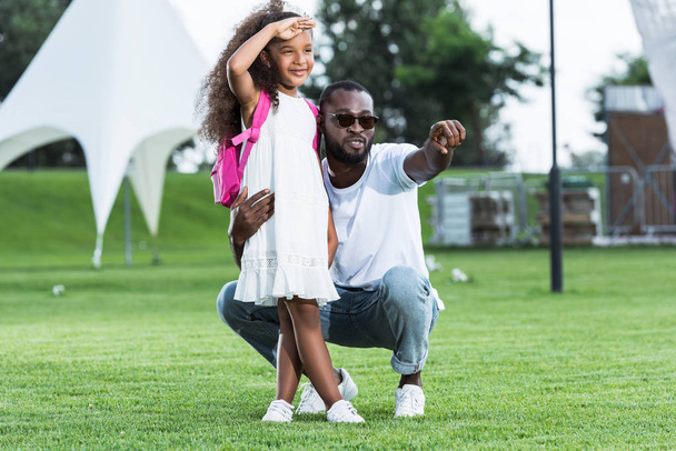 Afrikaanse Amerikaanse vader naar dochter met school tas in park op iets - Foto, afbeelding