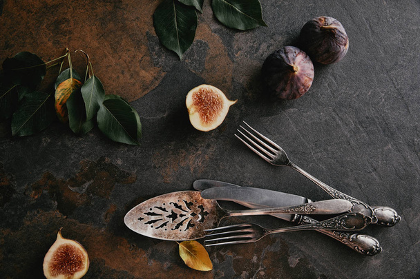 top view of antique cutlery, green leaves and figs on grungy surface - Photo, Image