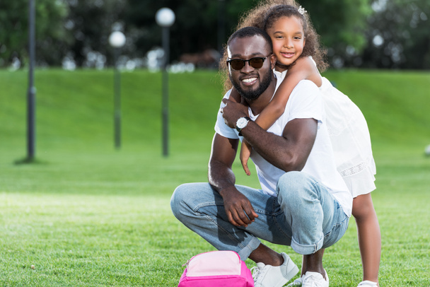 afro-américaine fille étreignant père de retour dans le parc, sac rose sur l'herbe
 - Photo, image