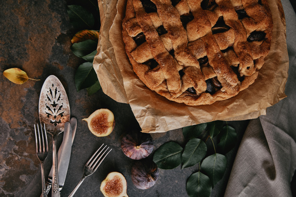flat lay with homemade pie on baking paper, antique cutlery and fresh figs on dark tabletop - Foto, Imagen