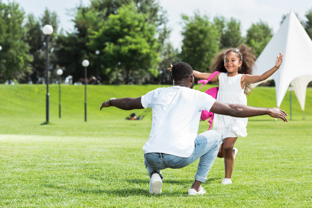 公園で両手を広げて父親に実行しているスクール バッグとアフリカ系アメリカ人の娘 - 写真・画像