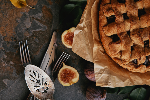 vista superior da torta caseira em papel manteiga, talheres antigos e figos frescos na mesa escura
 - Foto, Imagem