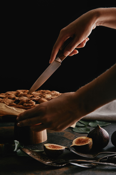bijgesneden schot van vrouw snijden taart op papier bakken met mes op oppervlak met vijgen - Foto, afbeelding