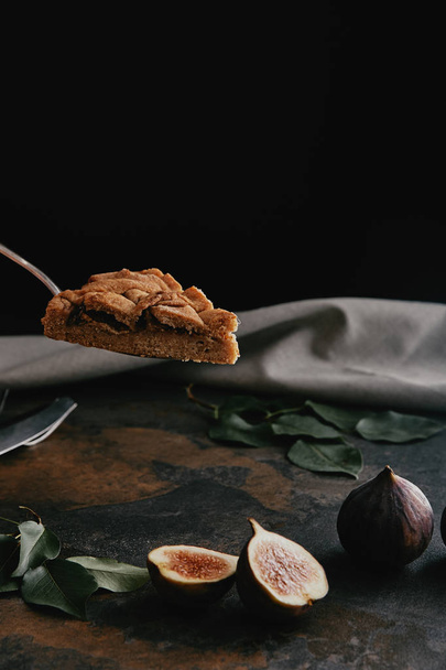 close up view of piece of pie on cake server and figs on dark grungy surface with black background - Photo, Image