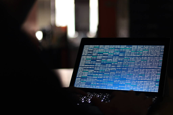 Computer Hacker siluetti kirjoittamalla tietokoneeseen pimeässä huoneessa. Työskentelen sinisen binäärikoodin parissa. binääritietojen, tietokoneohjelmoinnin ja verkkoturvallisuuden käsitteet
. - Valokuva, kuva