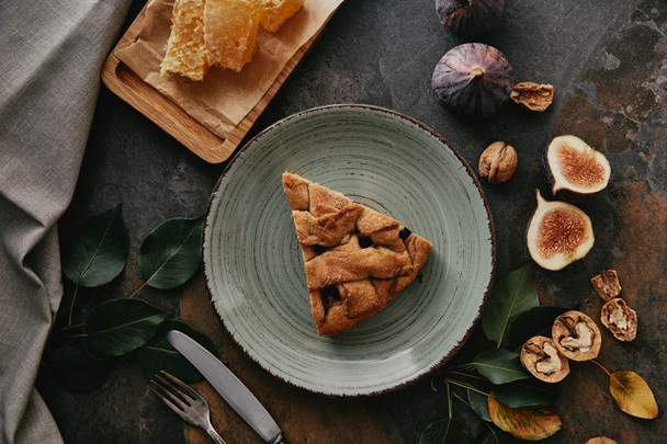 flat lay with piece of pie on plate, beeswax, figs and cutlery on grungy tabletop - Foto, immagini