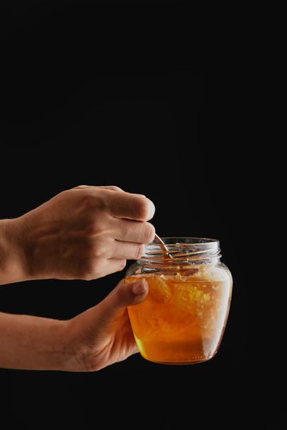 Μερική άποψη της γυναίκας που κρατά ποτήρι με φυσικό μέλι που απομονώνονται σε μαύρο - Φωτογραφία, εικόνα